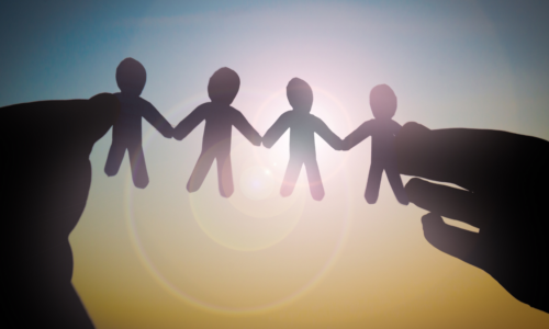 Silhouette of hands holding paper cutout figures of people in a chain, symbolizing unity and community. The image is backlit with a bright sunburst, creating a warm and hopeful atmosphere.